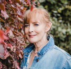 Author Deborah Jenkins, a middle aged woman with strawberry blonde hair and a denim jacket, smiling at the camera