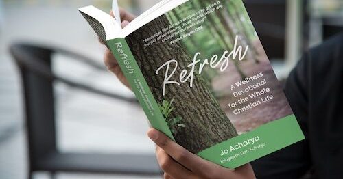 A man sits outside reading Jo Acharya's book 'Refresh: a wellness devotional for the whole Christian life'