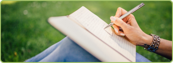 Image link for Blog showing a close up of a person writing in a notebook while sitting on grass