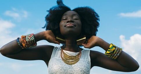 A black woman with afro hair and coloured bracelets developing a habit of thanksgiving by praising God against a blue sky
