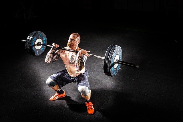 A bearded man with tattoos holds up a heavy barbell showing how strong he is
