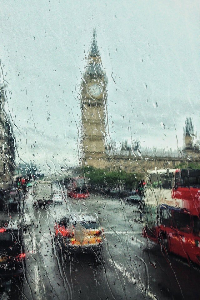 Looking through a wet window at a scene of London in the rain, with Big Ben and cars on the road in the foreground
